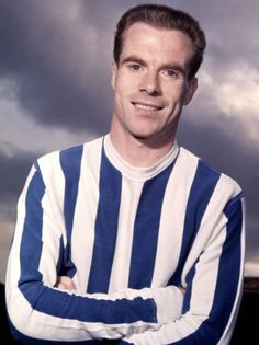 a man wearing a blue and white striped shirt with his arms crossed looking at the camera