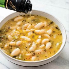 a white bowl filled with beans and broccoli next to a bottle of wine