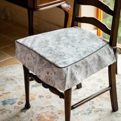 a chair with a flowered seat cover sitting on a rug in front of a window