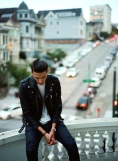 a young man sitting on the edge of a railing looking down at traffic in the distance