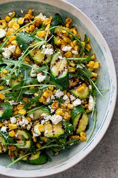 a bowl filled with cucumber, corn and feta cheese on top of it