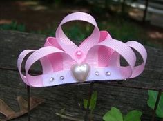 a pink tiara with pearls and a heart on the front is sitting on a fence