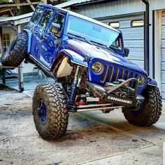 a blue jeep is parked in front of a garage with its lifted off wheel drive