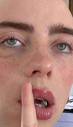 a woman with freckles on her face is holding her finger to her mouth