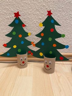 two christmas trees made out of toilet paper on top of a wooden table next to a wall