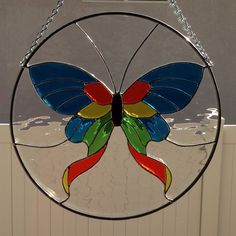 a colorful stained glass butterfly hanging from a chain on a window sill in front of a white wall