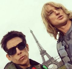 two men standing next to each other in front of the eiffel tower with sunglasses on