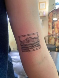 a small tattoo on the arm of a woman with mountains in the background and a stamp