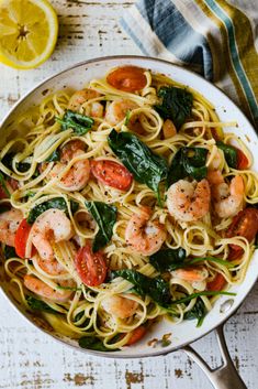 pasta with shrimp, spinach and tomatoes in a skillet on a white wooden table