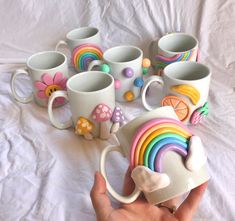 a hand holding a coffee cup with rainbow decorations on it and many mugs in the background