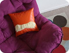 a purple chair with an orange and white pillow on it next to a colorful rug