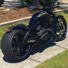 a black motorcycle parked on the side of a road next to a tree and grass