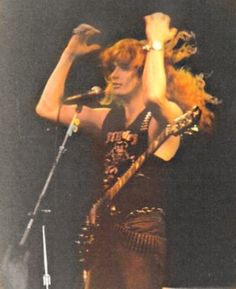 a woman holding a microphone on stage with her hands up in the air while singing