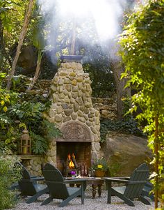 a fire place in the middle of a garden with chairs around it and a table surrounded by greenery