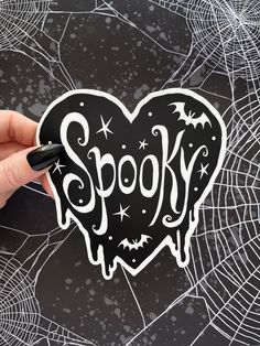 a hand holding a sticker with the word spook on it in front of a spider web