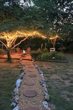 a stone path in the middle of a yard with lights strung over it and trees