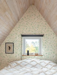 a bed sitting under a window in a bedroom next to a wooden wall and ceiling