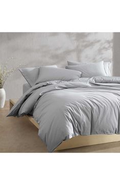 a bed with grey sheets and pillows on top of it in a room next to a plant