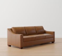 a brown leather couch sitting on top of a hard wood floor next to a white wall