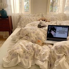 an open laptop computer sitting on top of a bed covered in white sheets and pillows