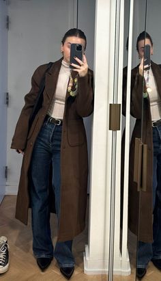 a woman taking a selfie in front of a mirror with her cell phone and coat on