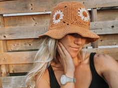 a woman wearing a brown hat with white flowers on the brim and her hand near her face