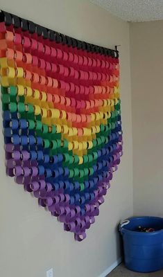 a rainbow colored wall hanging made out of toilet paper rolls in a room next to a blue bucket