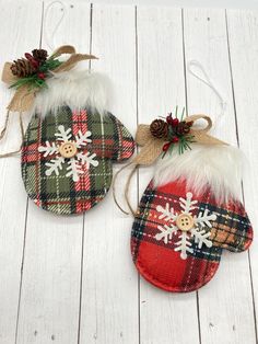 two plaid christmas mitts with snowflakes and pine cones on them sitting on a white wooden surface