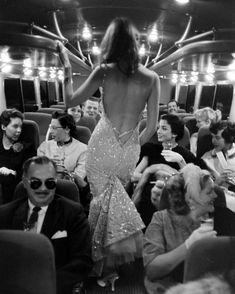 the back of a woman in a dress walking on a train with people sitting around