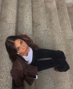 a woman is sitting on the stairs with her cell phone in her hand and looking up