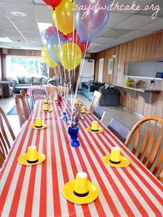 the table is decorated with yellow and red striped tablescloths, plates, and balloons