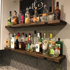 the shelves are filled with liquor bottles and empty glasses on it's sides, as well as a chalkboard that says after