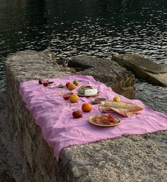 a table with food on it sitting next to the water in front of some rocks