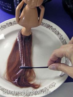 a person is painting a doll's hair on a plate