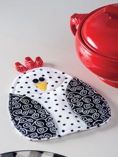 a red pot holder with a black and white chicken on it next to a plate