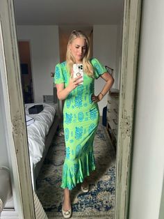 a woman in a green dress taking a selfie with her cell phone while standing in front of a mirror