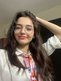 a woman wearing glasses and a tie is standing in front of a mirror with her hand on her head