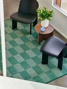 two black chairs and a small table in a room with green rugs on the floor