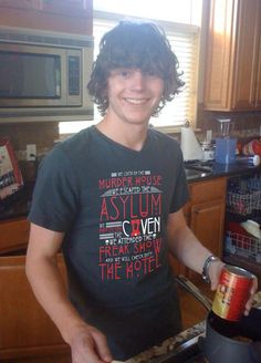 a young man holding a can of beer in his hand while standing next to an oven