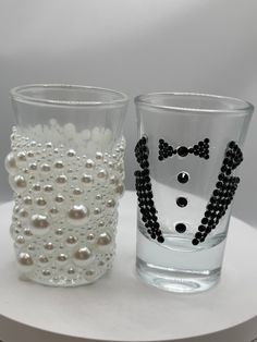 two shot glasses with pearls on them are sitting on a white table and one has a bow tie