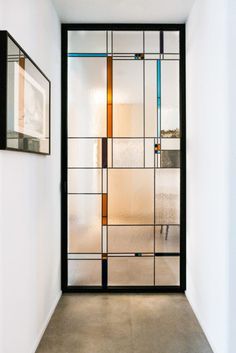 an empty hallway with a glass door and framed pictures on the wall above it, in front of a white wall