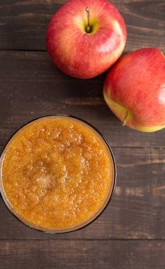 two apples and a glass of apple cider on a wooden table