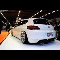 the rear end of a white car parked in a showroom with other cars on display