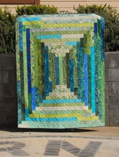 a green and blue quilt sitting on top of a cement wall next to a planter