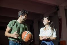 a man standing next to a woman holding a basketball in her hand and smiling at each other