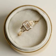 an engagement ring in a box on a white surface with gold trimming and diamond accents