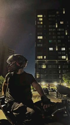 a man riding a motorcycle at night in front of a tall building with lots of windows
