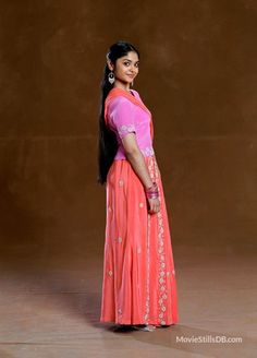 a woman in an orange and pink sari poses for a photo with her hands on her hips