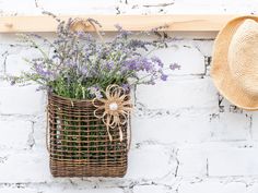 a basket filled with lavender flowers next to a hat hanging on a white brick wall