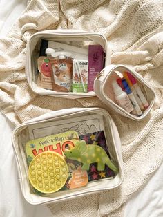 two plastic containers filled with toys on top of a white blanket next to each other